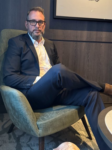 Portrait of James R. Bateman (James Bateman): a man wearing a blue suit with a white shirt. He is wearing glasses and his leg is crossed. His hair is slightly parted with a beard